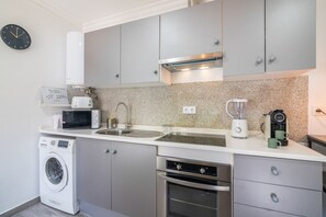 A compact kitchen with a washing machine, microwave, sink, and a coffee maker.