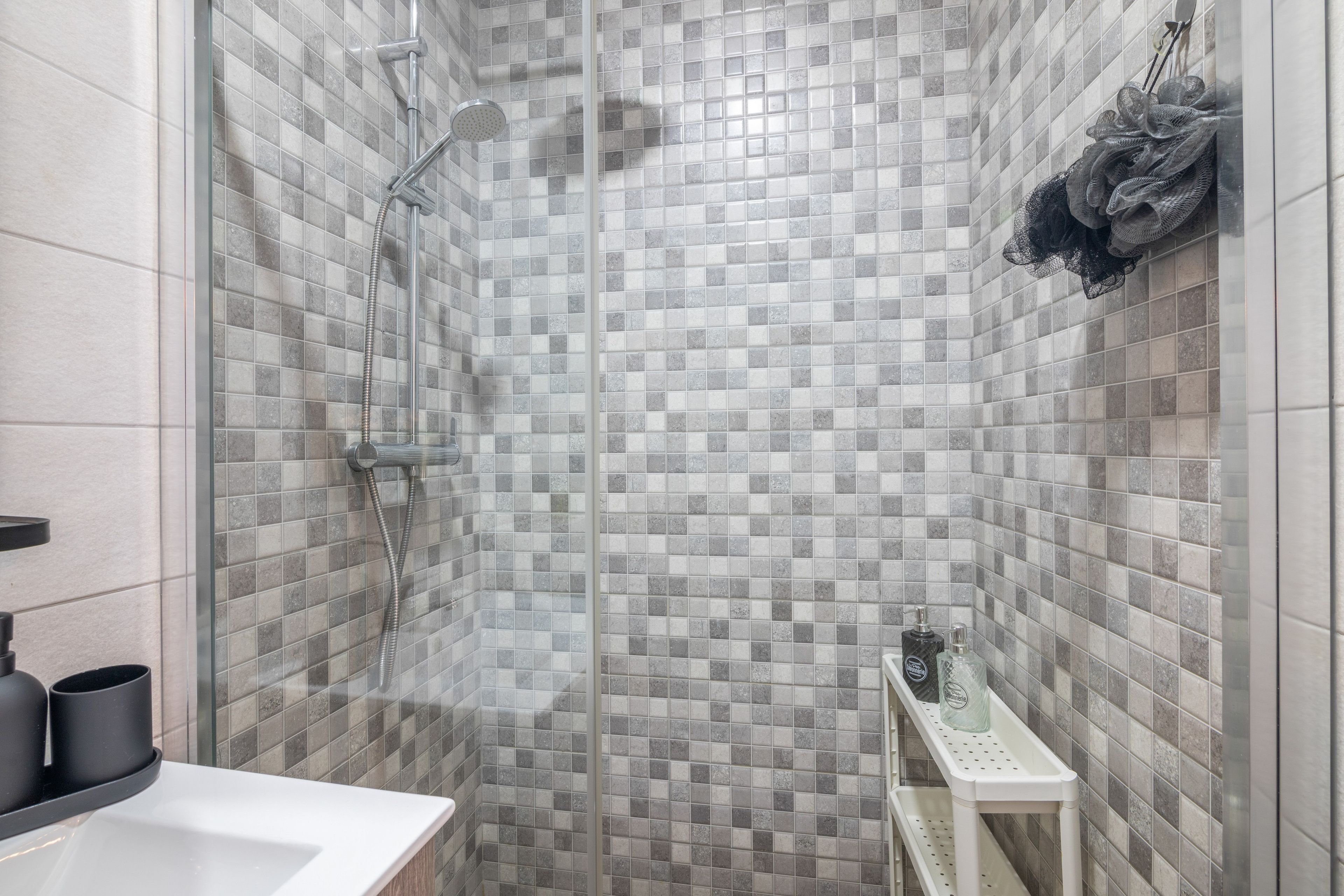 Eine Dusche mit Glastür, geflieste Wände und einem Ablagefach für Pflegeprodukte.