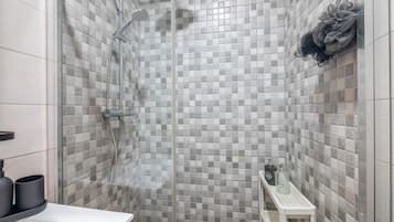 Eine Dusche mit Glastür, geflieste Wände und einem Ablagefach für Pflegeprodukte.