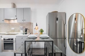 A modern kitchen with a built-in oven, a stainless steel refrigerator, and a dining table with chairs.