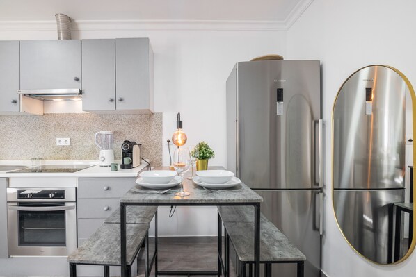 A modern kitchen with a built-in oven, a stainless steel refrigerator, and a dining table with chairs.