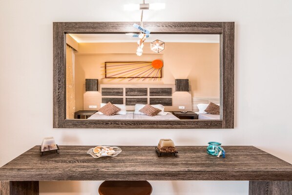 A hotel room with a large mirror, a wooden bedside table with decorative items, and a bed with a headboard.