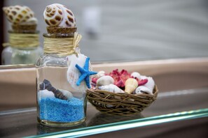 A glass bottle with a cork stopper, containing blue sand and a starfish, next to a wicker basket with seashells and a starfish.