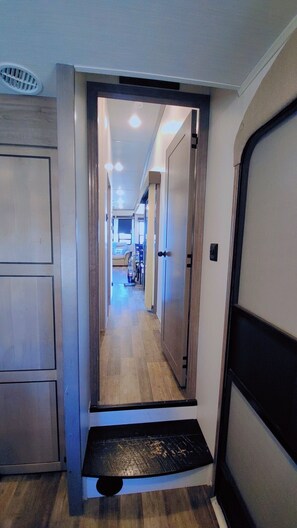 Un corridoio con pavimento in legno, una porta che conduce a una stanza e una bocchetta di ventilazione sul soffitto.