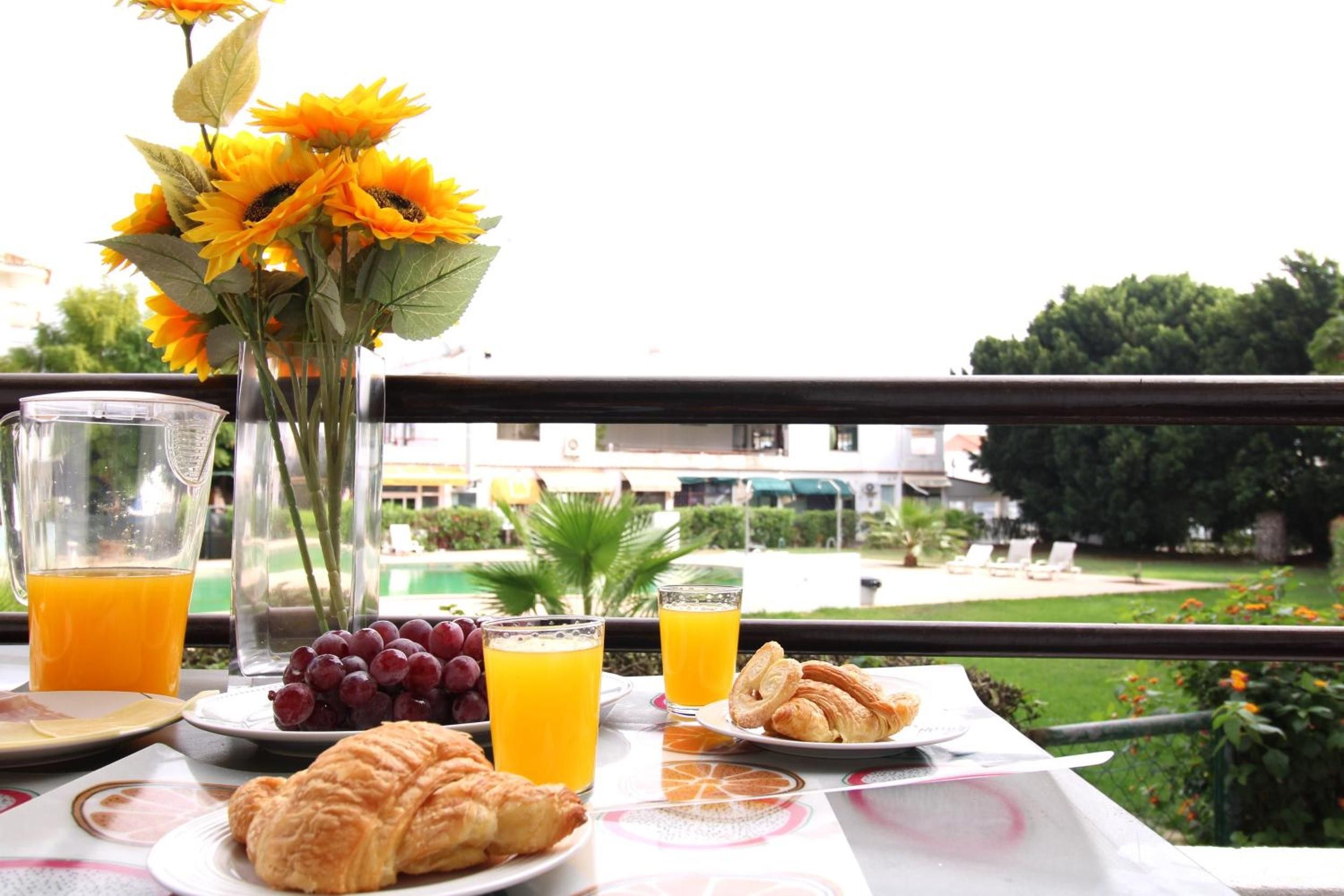 Una mesa de desayuno con cruasanes, uvas, jugo de naranja y un jarrón de girasoles.