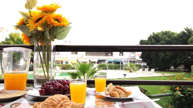 Une table de petit-déjeuner avec des croissants, des raisins, du jus d’orange et un vase rempli de tournesols.