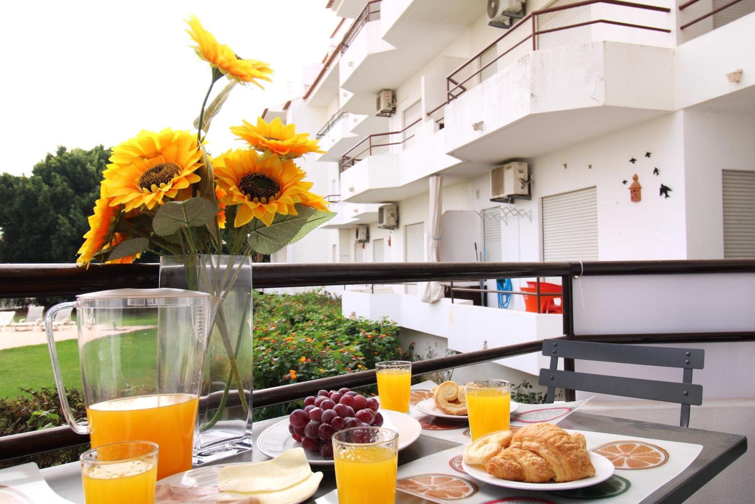 Una mesa de desayuno con un jarrón de girasoles, un plato de uvas, croissants y vasos de jugo de naranja.
