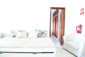 Un dormitorio con una cama, un sofá blanco y una puerta que da a otra habitación.