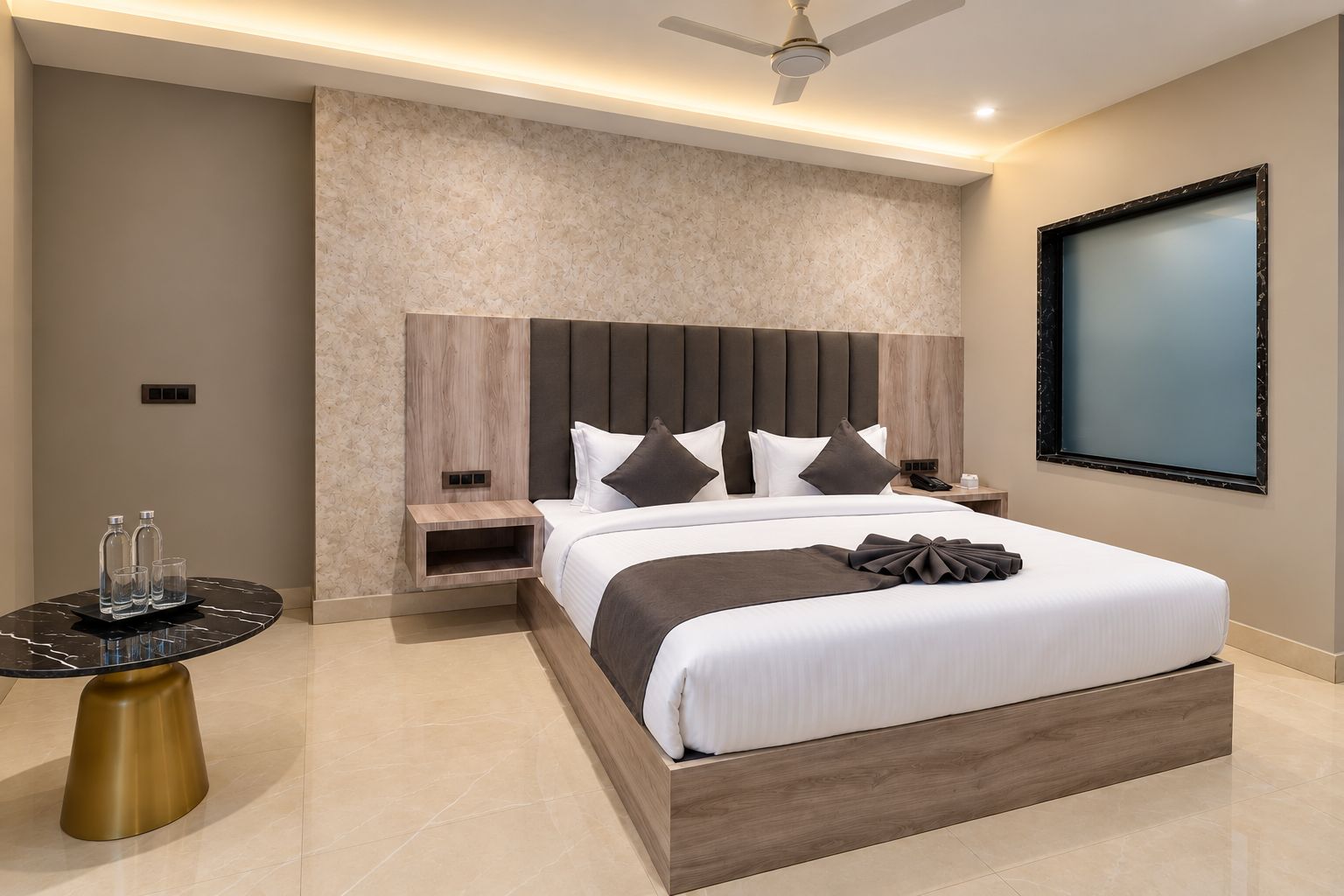 A modern hotel room with a large bed, a nightstand, a round table with a gold base, and a ceiling fan.