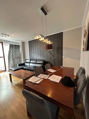 Een moderne woonkamer met een houten eettafel, een zwarte leren bank en een bijzondere geometrische hanglamp.