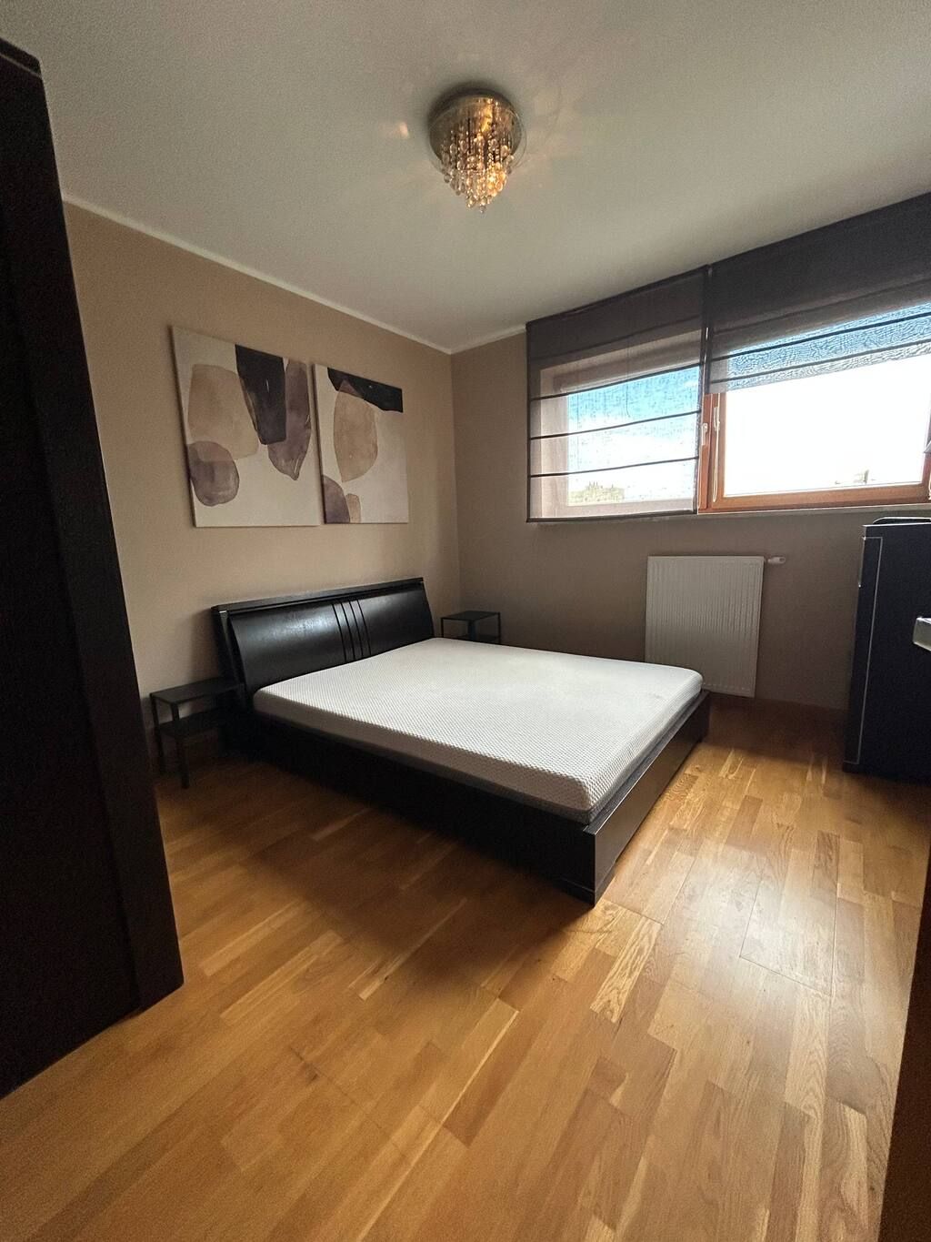 A bedroom with a bed, a radiator, a window, and artwork on the wall.
