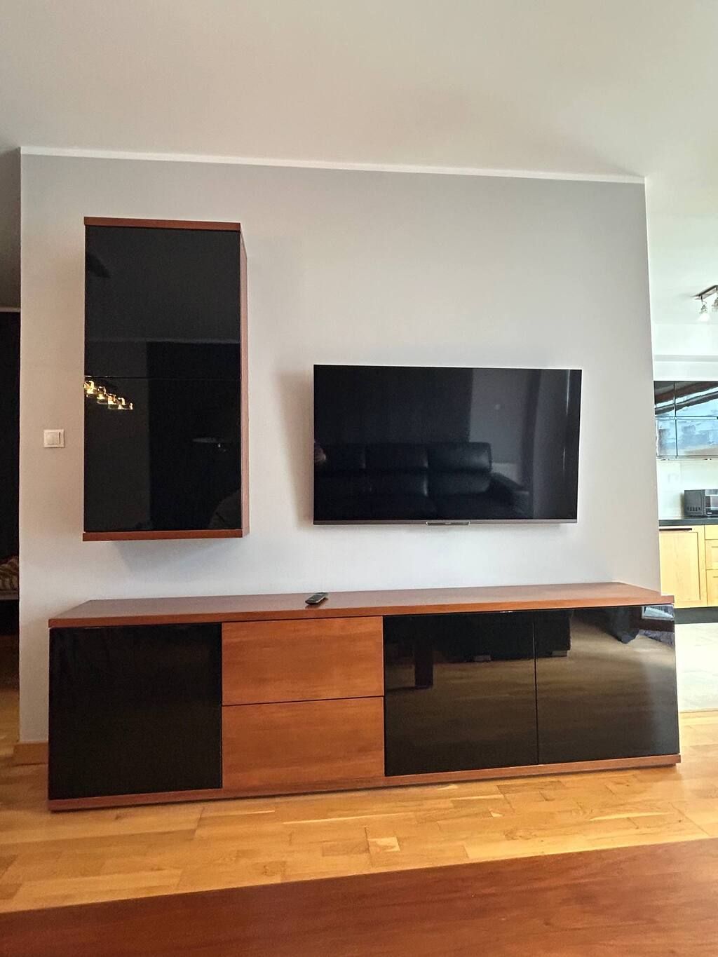 Un'elegante mobile TV moderno con televisore a schermo piatto montato su una parete bianca, un armadietto in legno sottostante e un piccolo telecomando sullo scaffale superiore.
