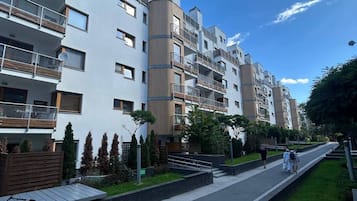 A multi-story residential building with balconies, a paved walkway, and greenery.