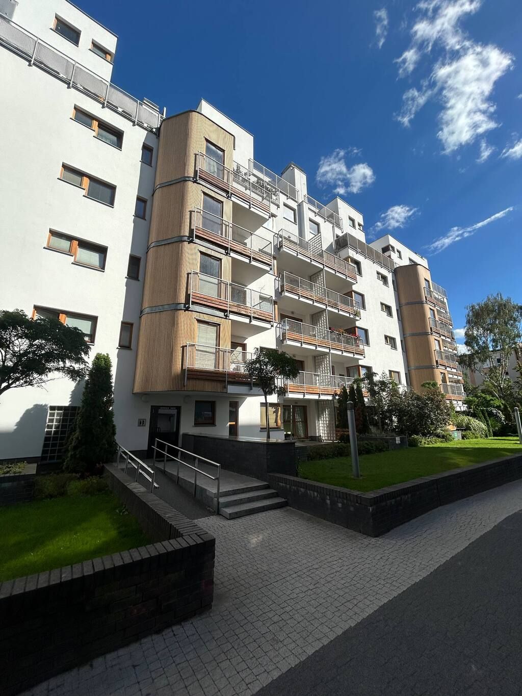 A multi-story residential building with balconies, a gated entrance, and a landscaped garden area.