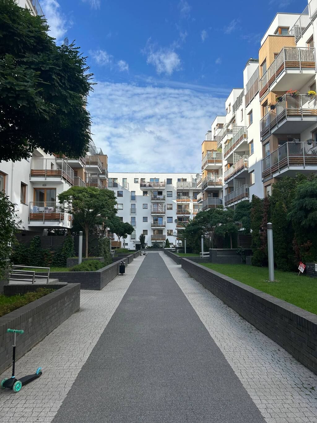 A pathway leading to a modern apartment complex with multiple balconies and a clear sky.