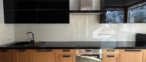 A modern kitchen with a black countertop, wooden cabinets, and stainless steel appliances.