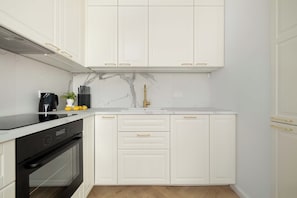 Una cucina con mobili bianchi, un piano cottura nero e uno schienale in marmo.