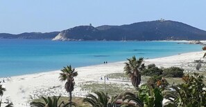 Uma praia com águas azul-claras, areal dourado e uma colina ao fundo.