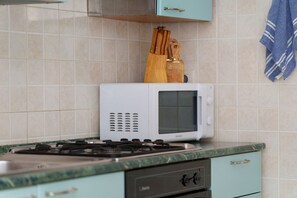 Cozinha com micro-ondas branco, fogão a gás e utensílios de madeira no balcão.
