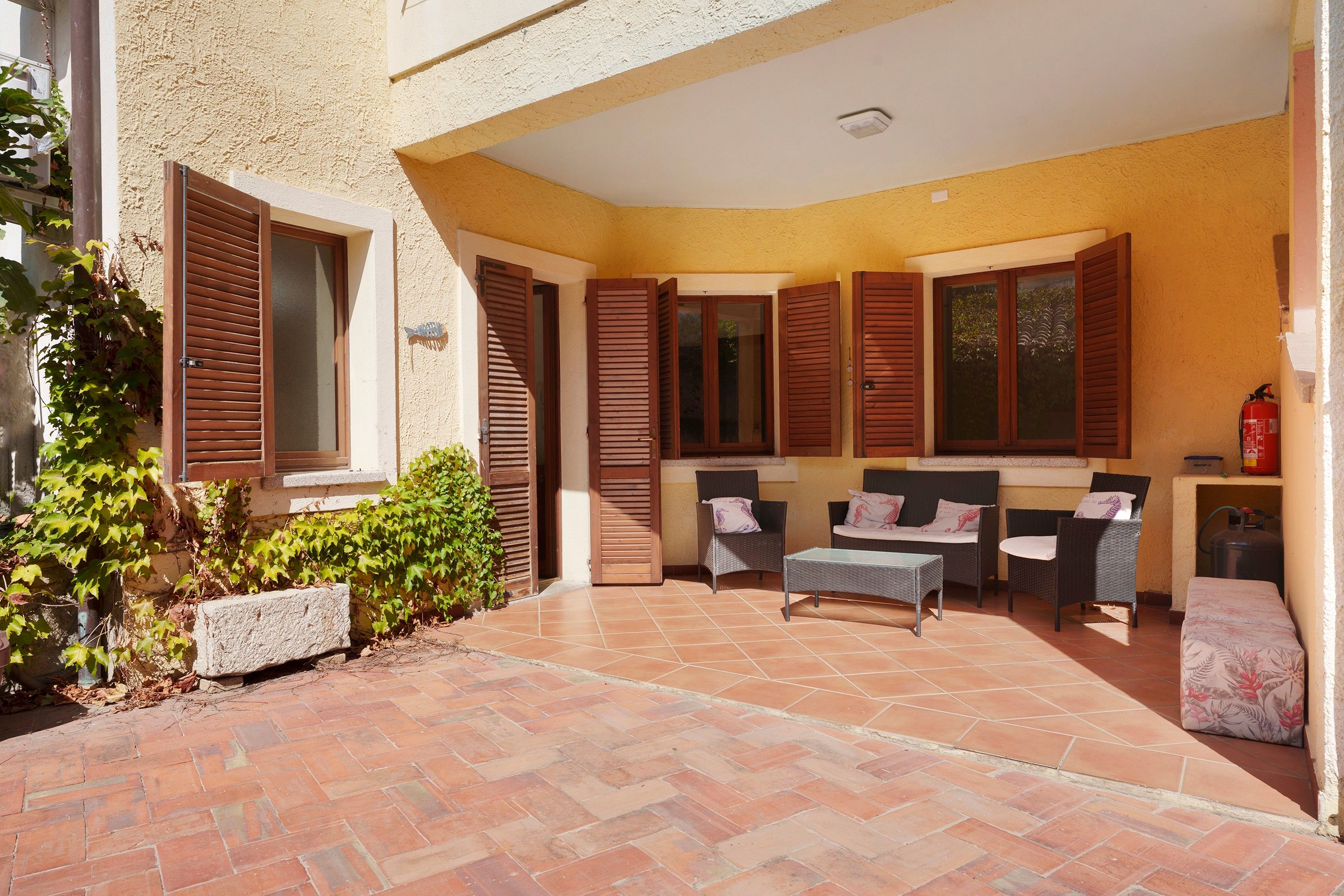 A covered patio area with outdoor furniture, a fire extinguisher, and a fire hose.