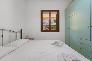 Quarto com uma cama de solteiro, janela, mesa de cabeceira e guarda-roupa.