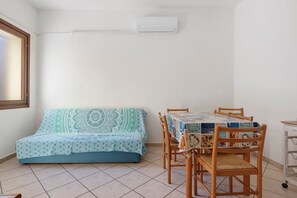 A small room with a sofa, a dining table with chairs, and an air conditioning unit on the wall. - Gamm Simius Home Holiday 1 (Villasimius)
