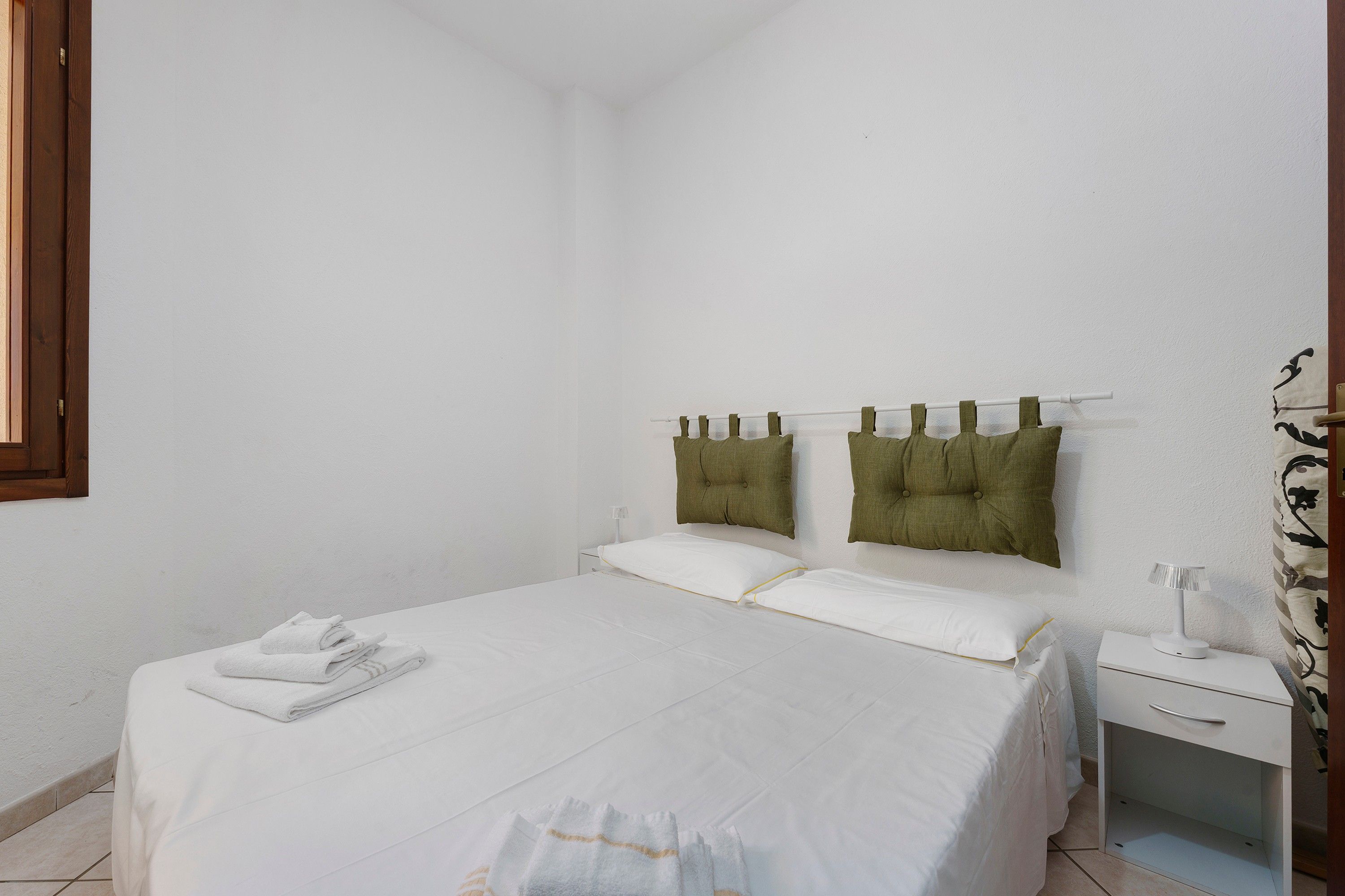 Un dormitorio con cama, almohadas, mesita de noche y lámpara.