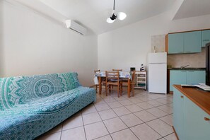 Ein kompakter Wohnbereich mit Sofa, Esstisch, Stühlen, einer Küchenzeile mit Schränken und einem Deckenventilator.