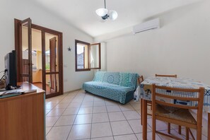 A room with a sofa, a dining table with chairs, a TV, and an air conditioning unit. - Gamm Simius Home Holiday 2 – Central Apartment for Families and Friends (Villasimius)