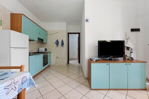 Eine kleine Küche mit türkisfarbenen Schränken, einer Mikrowelle und einem Kühlschrank.
