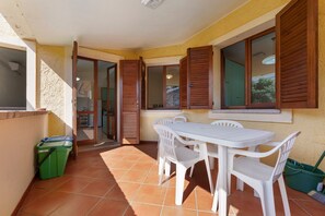 Un espace patio comprenant une table et des chaises, une poubelle et une porte-fenêtre coulissante donnant sur un espace intérieur.