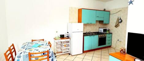 A compact kitchen with teal cabinets, a white refrigerator, and a dining area with a table and chairs.