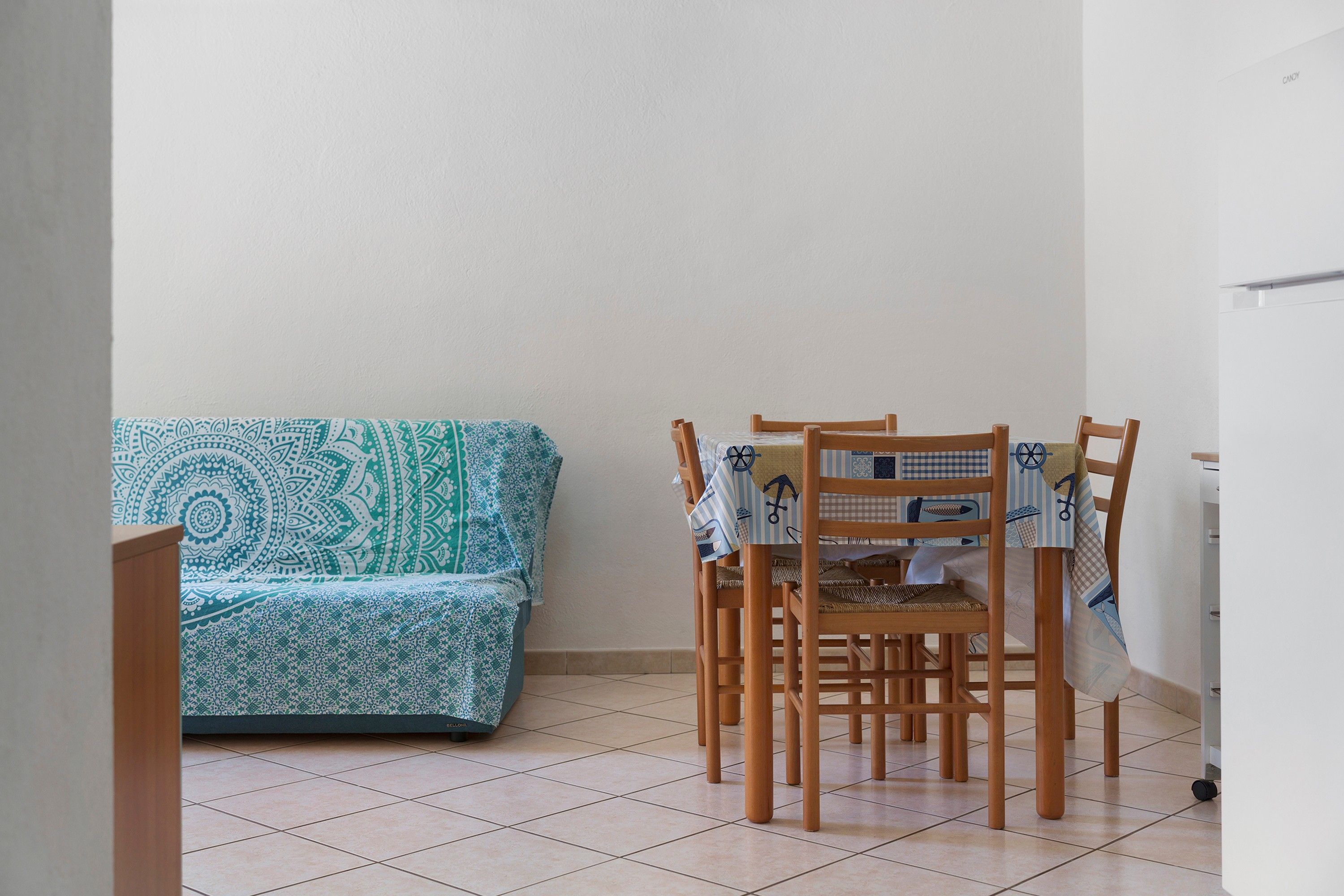 Une pièce avec un canapé à motifs, des chaises en bois et un sol carrelé.
