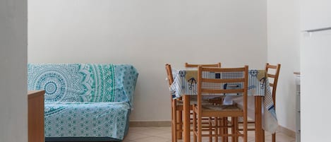 Une pièce avec un canapé à motifs, des chaises en bois et un sol carrelé.