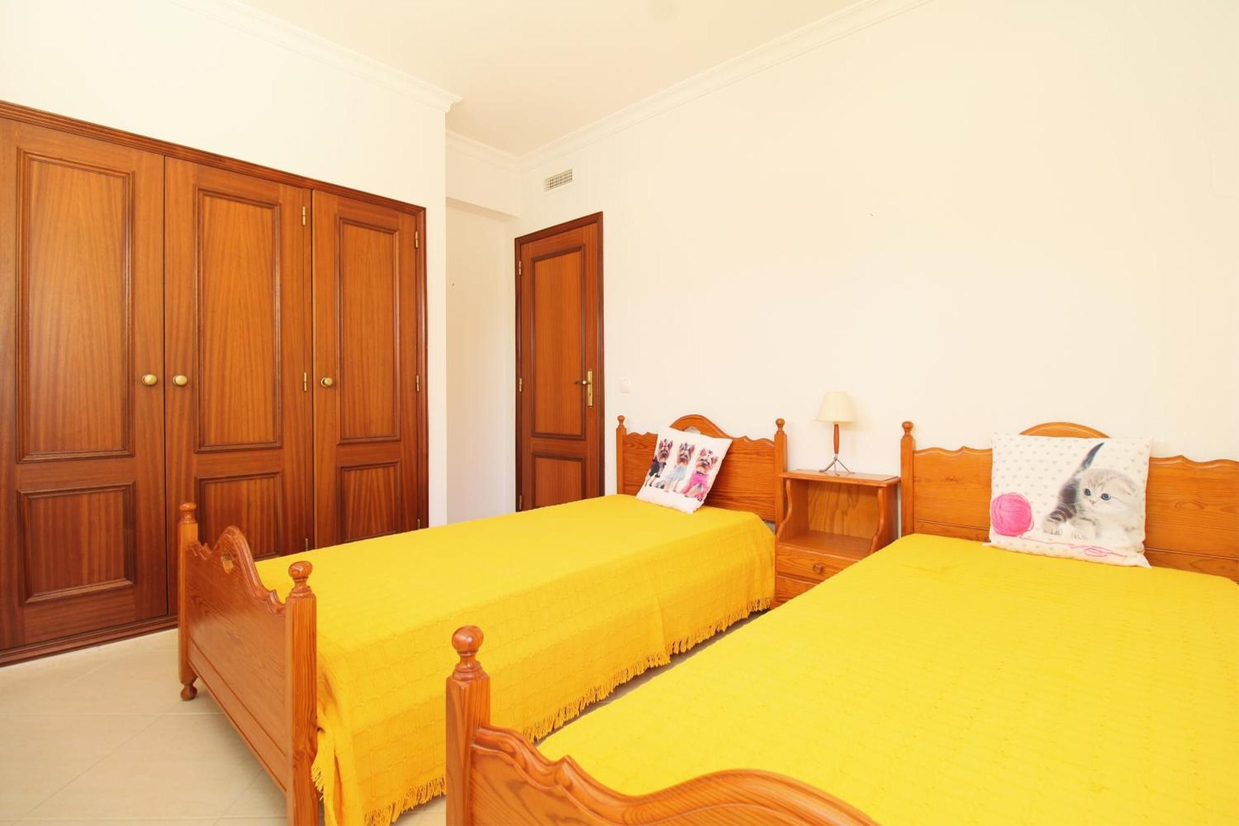Una habitación con dos camas individuales, armarios de madera y una mesita de noche con lámpara.