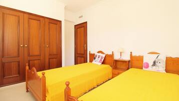 Una habitación con dos camas individuales, armarios de madera y una mesita de noche con lámpara.