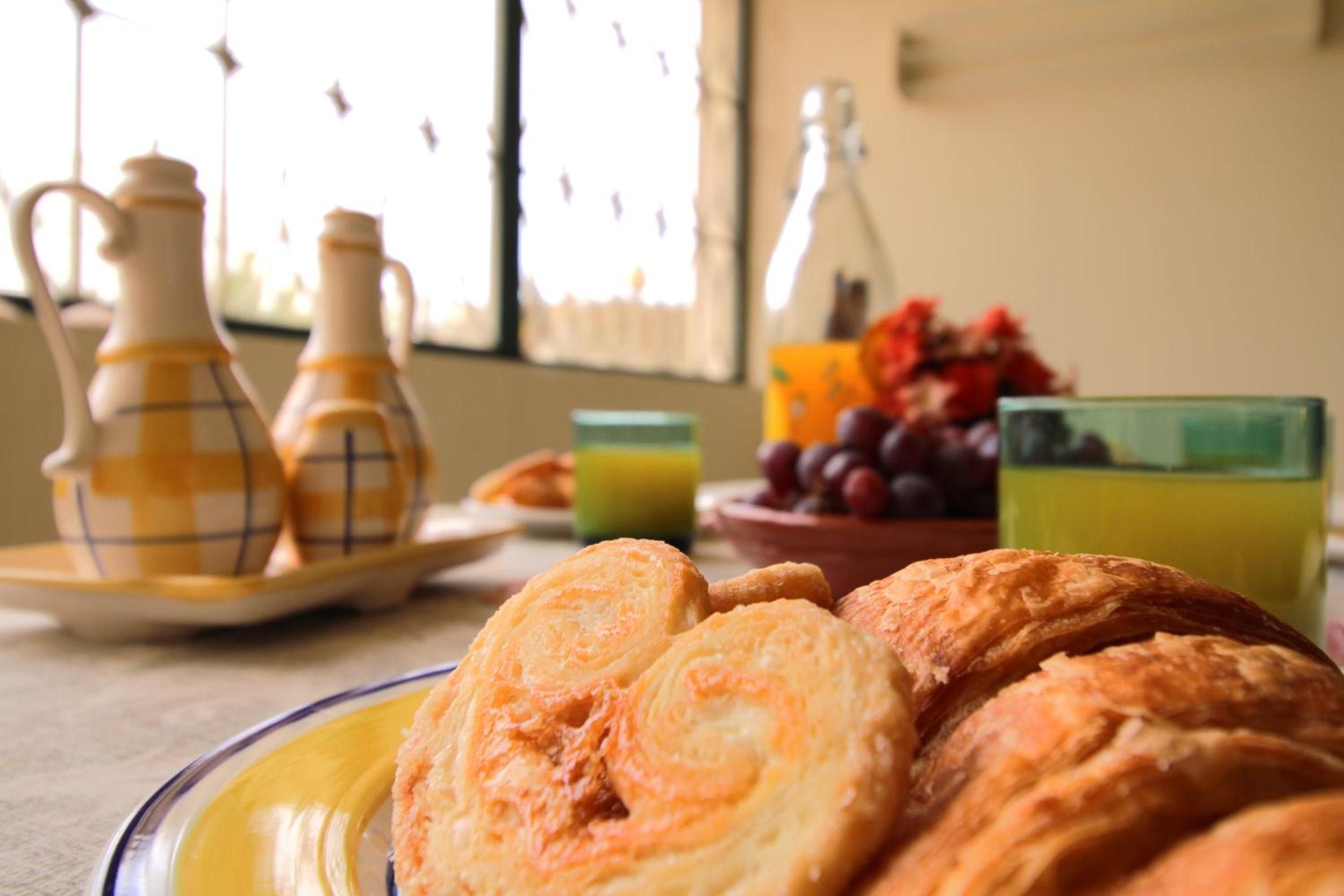 En frukostuppdukning med croissanter, en fruktskål och ett glas apelsinjuice på ett bord.