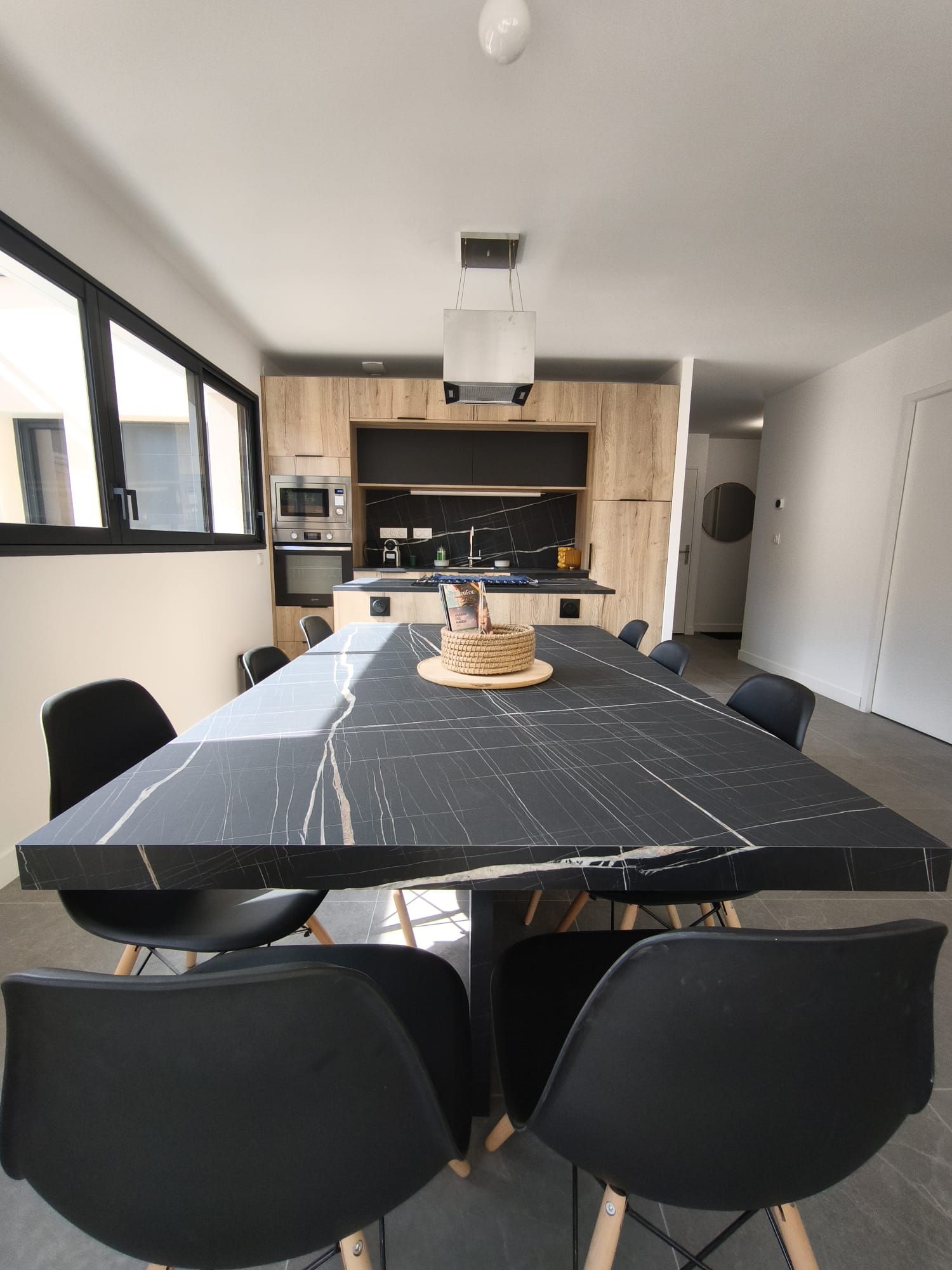 A modern kitchen with built-in appliances and a dining area with a marble table and black chairs.