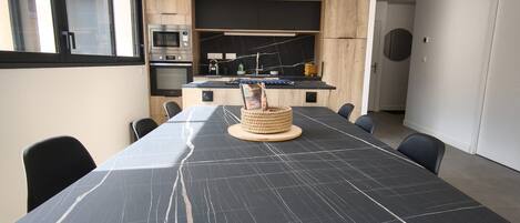 A modern kitchen with built-in appliances and a dining area with a marble table and black chairs.