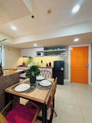 A modern kitchen with a dining area, including a table set for two, a microwave, and a refrigerator. - 2BR Modern Boho Suite (Parañaque)