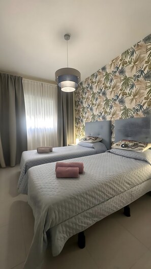 A hotel room with two beds, a large window with curtains, a ceiling light, and a tropical wallpaper. - Sea, comfort and tranquillity — right by the beach (Denia)