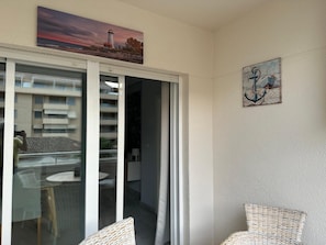 A balcony with a glass door, wicker furniture, and a painting of a lighthouse. - Sea, comfort and tranquillity — right by the beach (Denia)