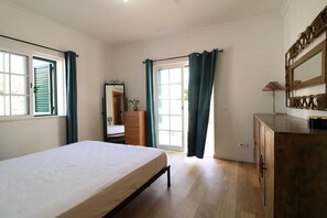 Ein Schlafzimmer mit einem Bett, einem Schminktisch, einem Spiegel und einer Tür zu einem anderen Raum.
