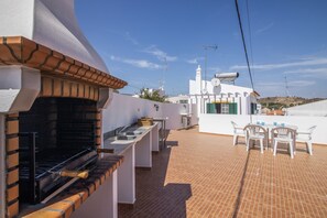 A rooftop terrace with a barbecue grill, outdoor seating, and a view of the surrounding landscape.