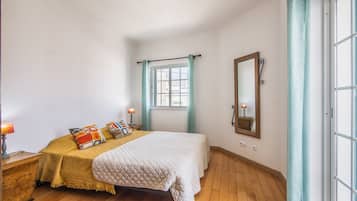 Une chambre à coucher avec un lit, des lampes de chevet, un miroir et une fenêtre avec des rideaux.