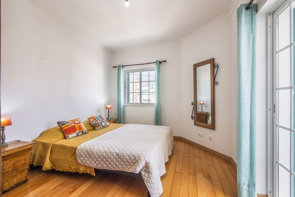 A bedroom with a bed, bedside lamps, a mirror, and a window with curtains.