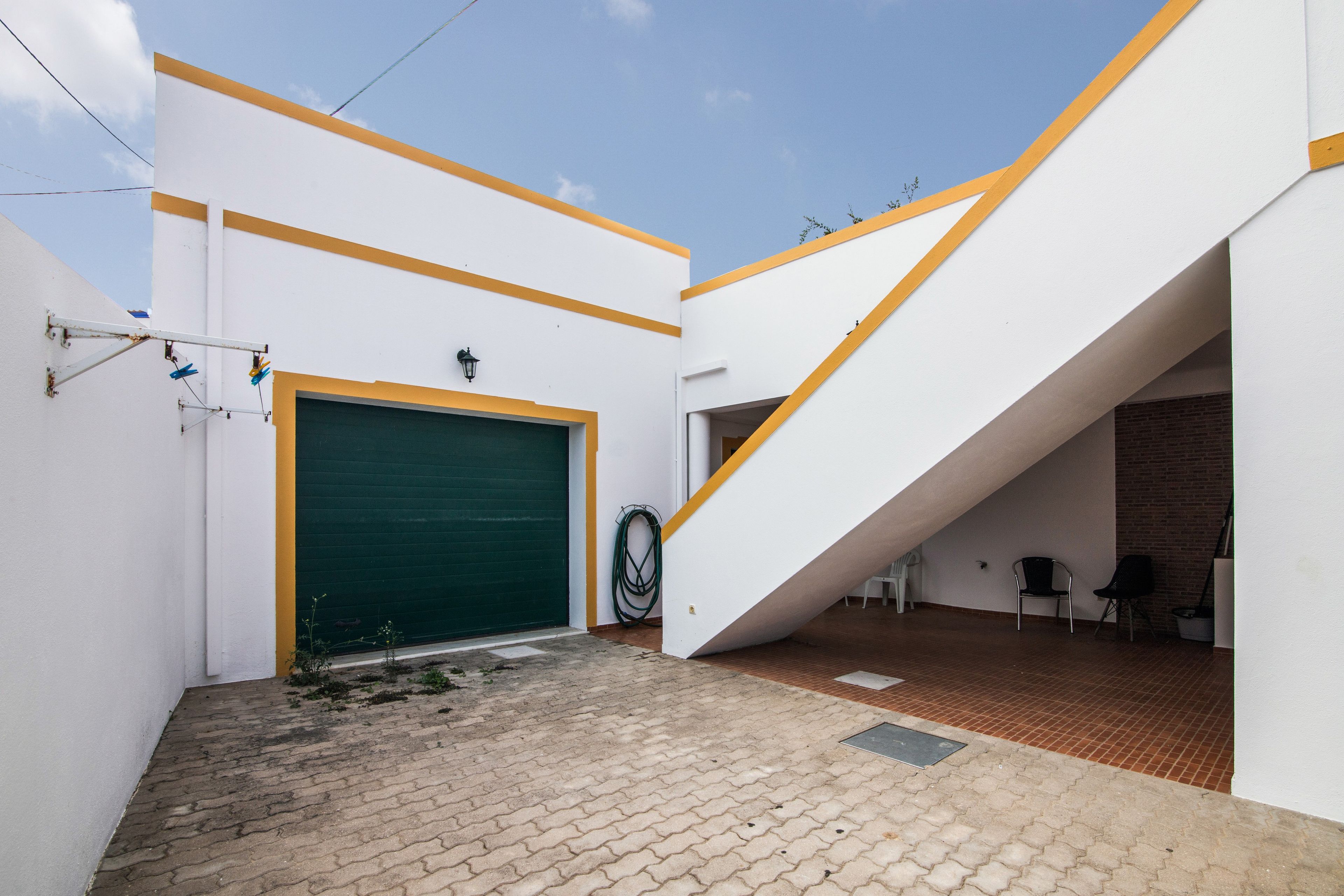 Ein Gebäude mit einer grünen Garagentür, einer weißen Fassade mit gelben Akzenten und einem Ziegelboden.