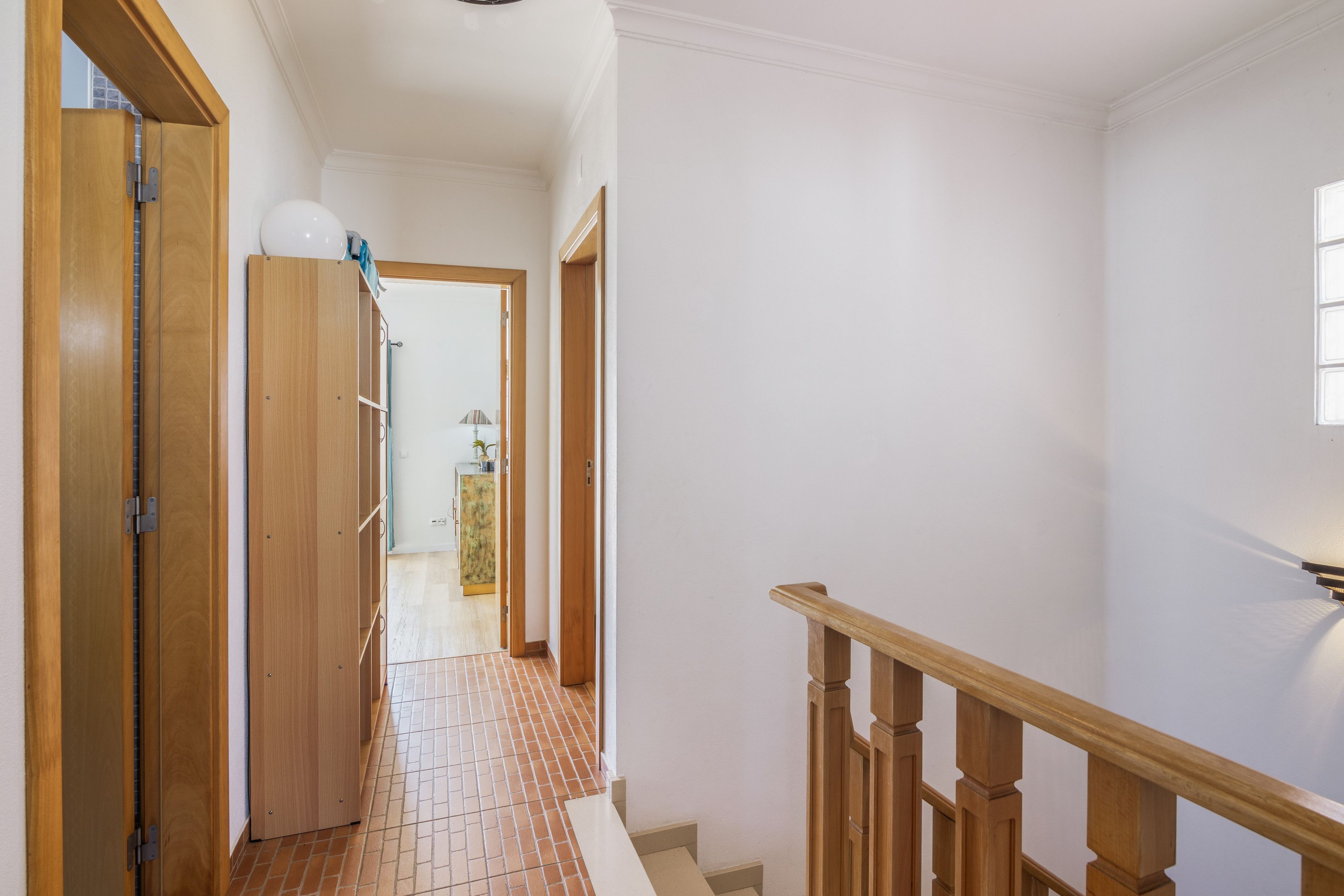 Un pasillo con puertas de madera, suelo de baldosas y una escalera con barandillas de madera.