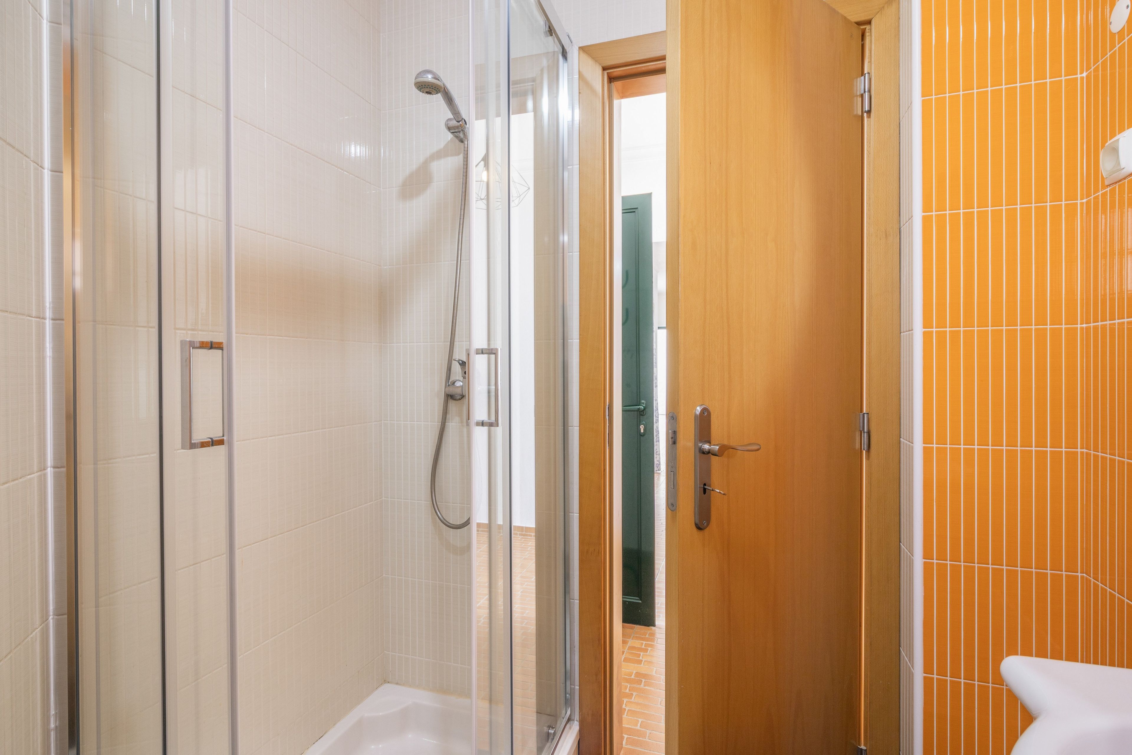 A bathroom with a glass-enclosed shower, a wooden door, and a tiled wall.