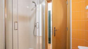 A bathroom with a glass-enclosed shower, a wooden door, and a tiled wall.